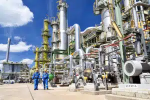 Chemical industry plant scene with refinery workers in protective work clothes inspecting piping systems and industrial