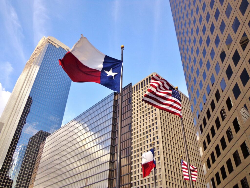Two flags—an American flag and a Texas state flag—flying prominently in downtown Houston, Texas